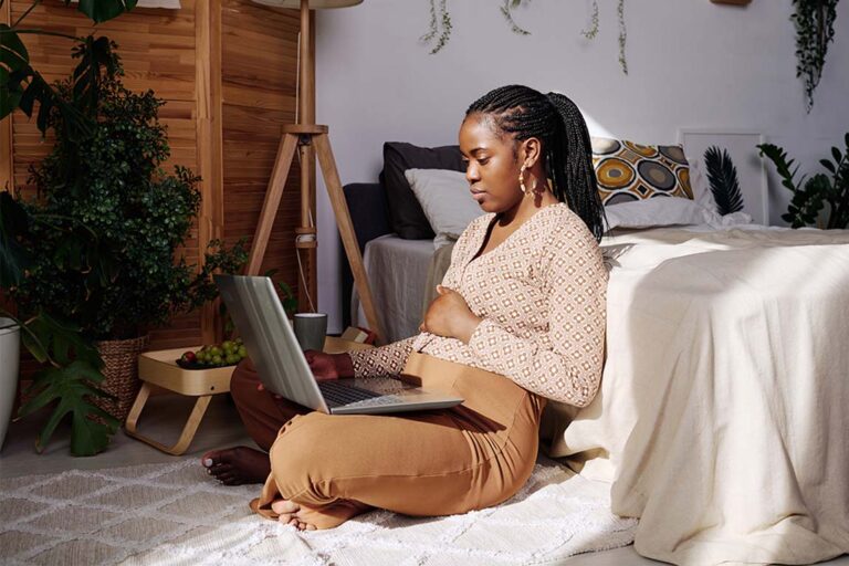 A person sits on the floor next to their bed and uses a laptop to research online therapy that takes insurance.
