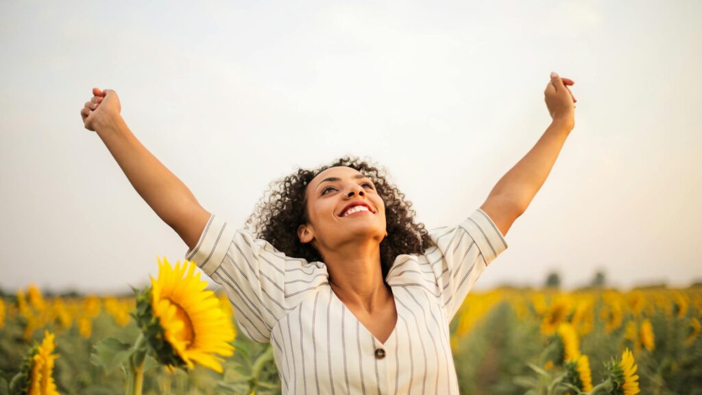 A woman stretches arms to the sky in a sunflower field.