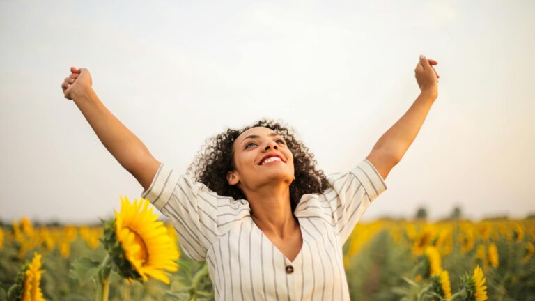 A woman stretches arms to the sky in a sunflower field.