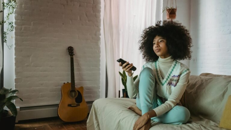 Woman on couch uses a remote to change the channel on her TV.