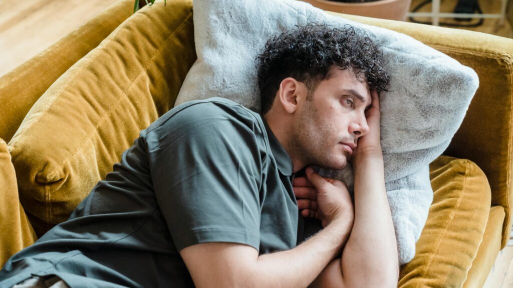 Man lies on couch looking depressed.