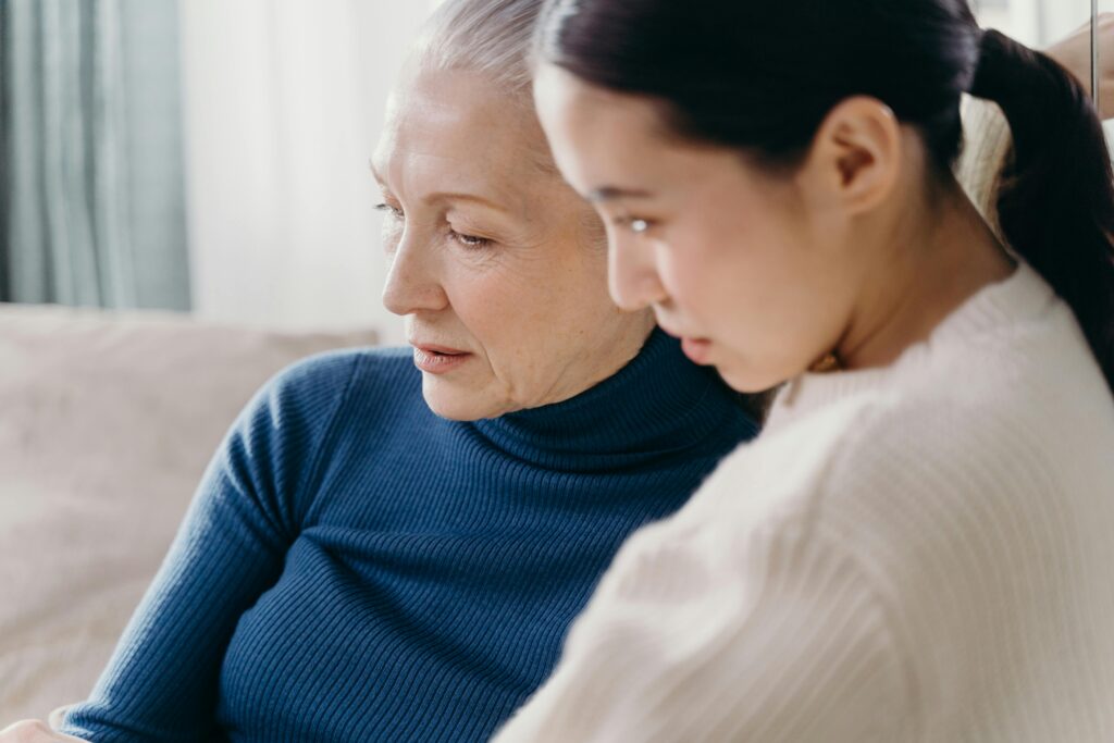 Three generations of women sitting on a couch together, looking at a book and smiling.