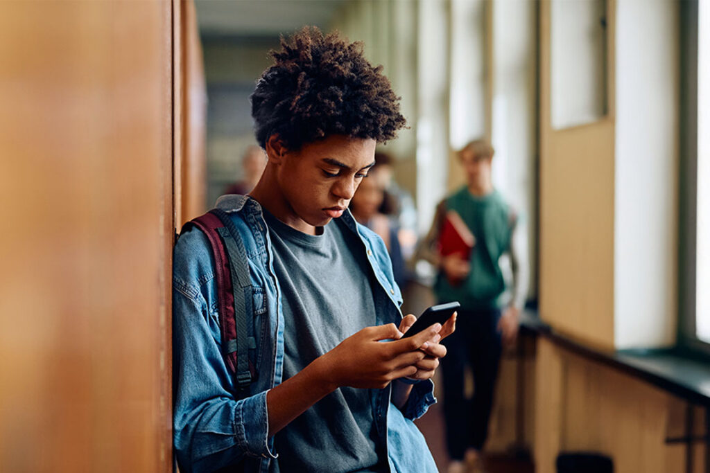 A student at school on his phone, looking concerned.