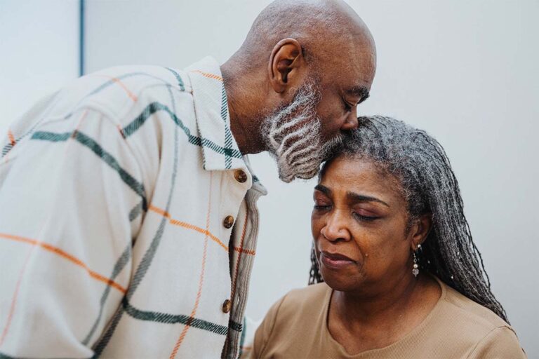 A man kisses his wife on the forehead as she grieves a loss.