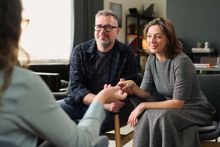 Photo of a man and woman holding hands while speaking with a couples therapist