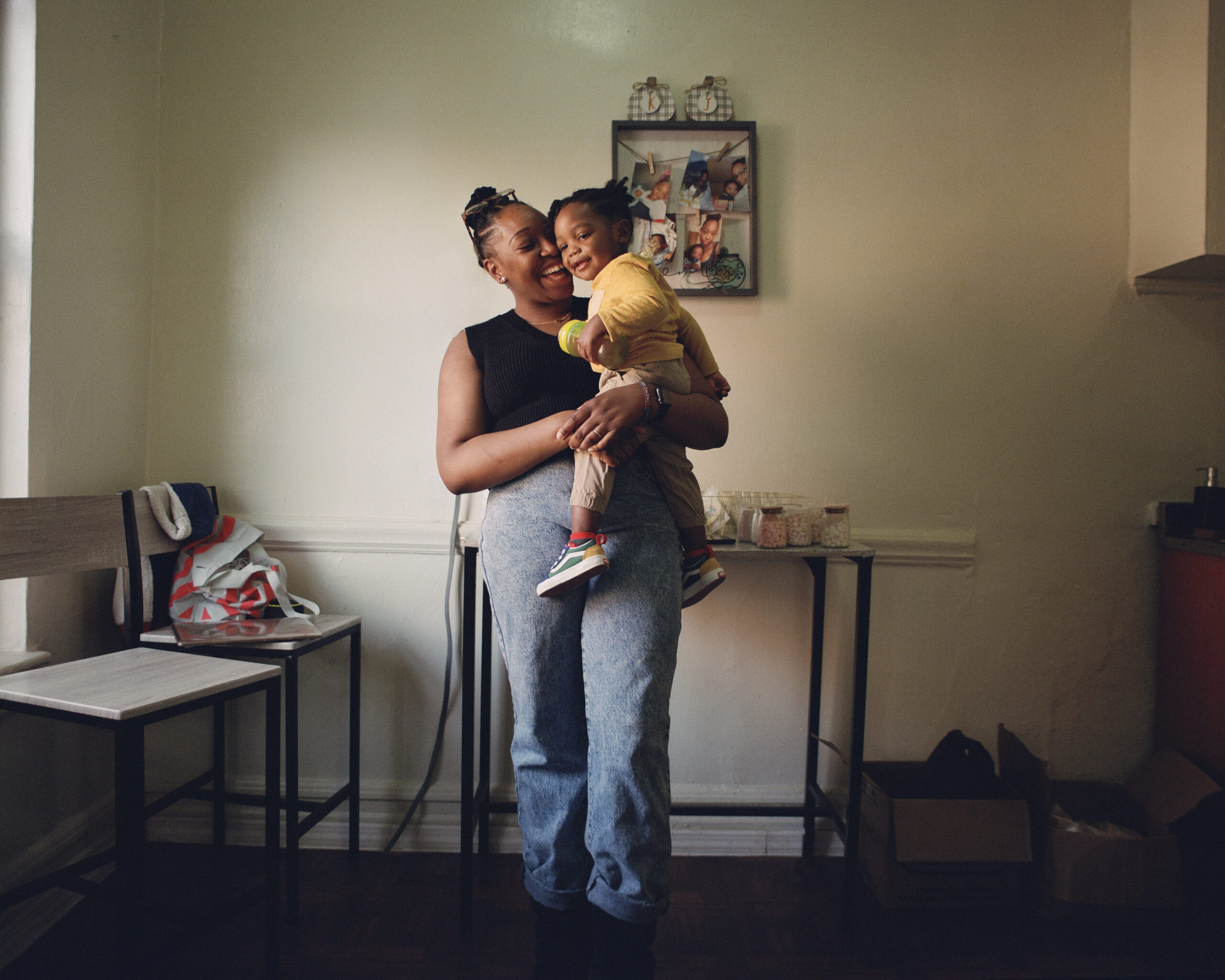 A woman lovingly holds a smiling child in a cozy room with soft lighting. The child wears a yellow outfit, evoking warmth and happiness.